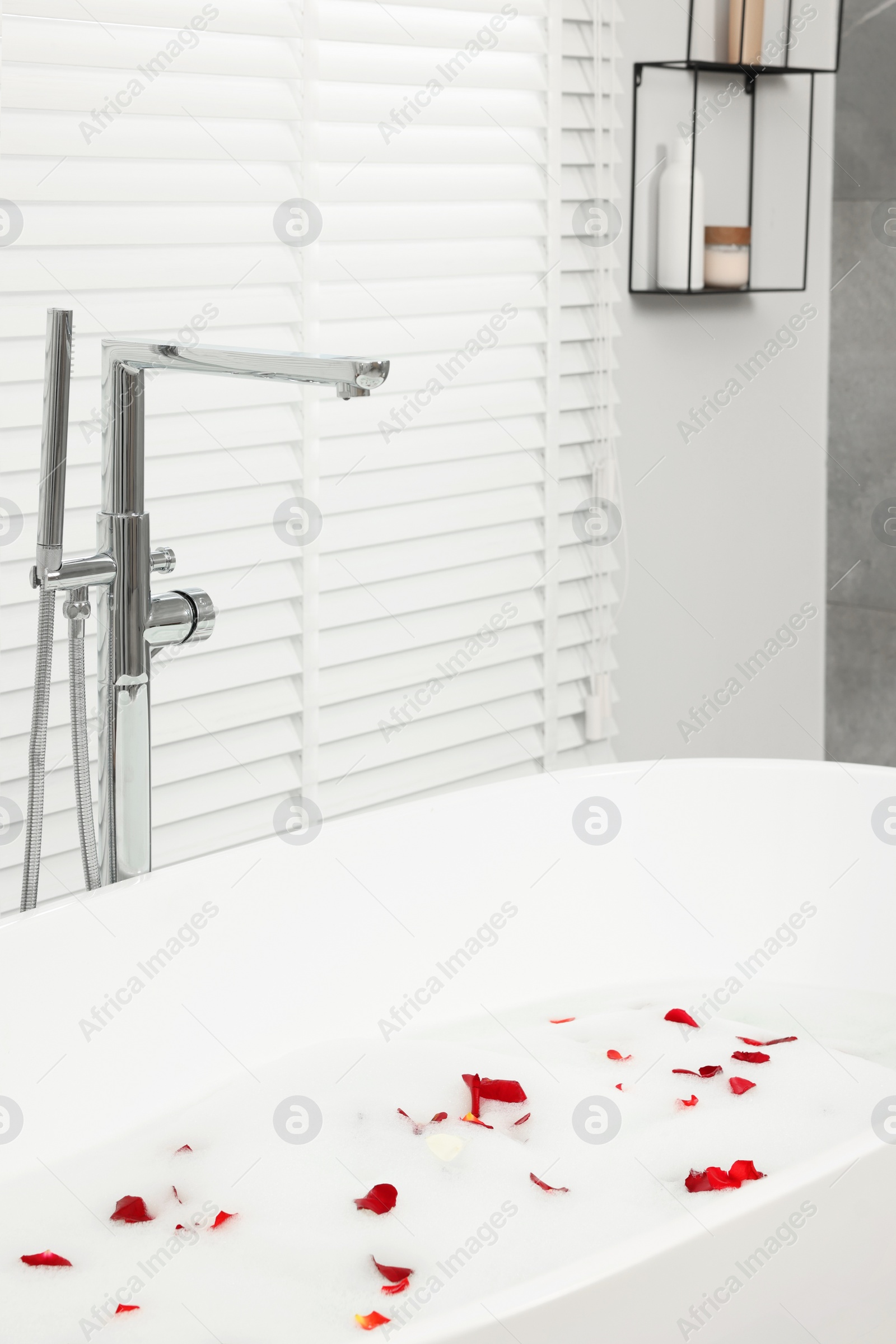 Photo of Bath tub with rose petals and foam in bathroom