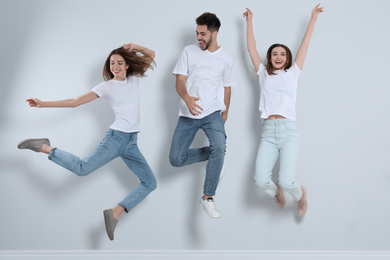 Photo of Group of young people in stylish jeans jumping near light wall