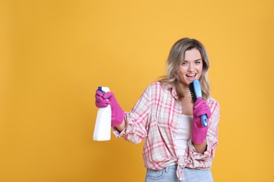 Photo of Beautiful young woman with brush and bottle of detergent singing on orange background. Space for text
