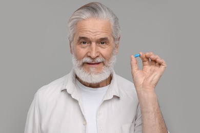 Senior man with pill on grey background