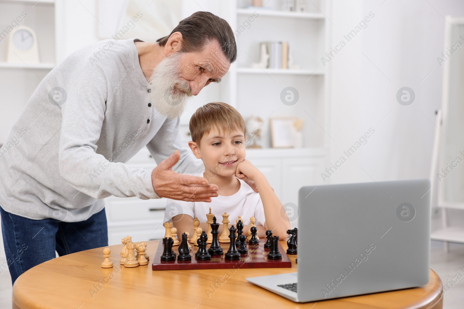 Photo of Grandfather teaching his grandson to play chess following online lesson at home