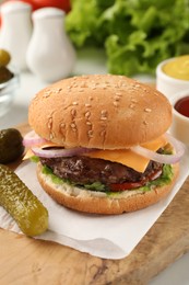 Tasty hamburger with patty, cheese and vegetables on wooden board