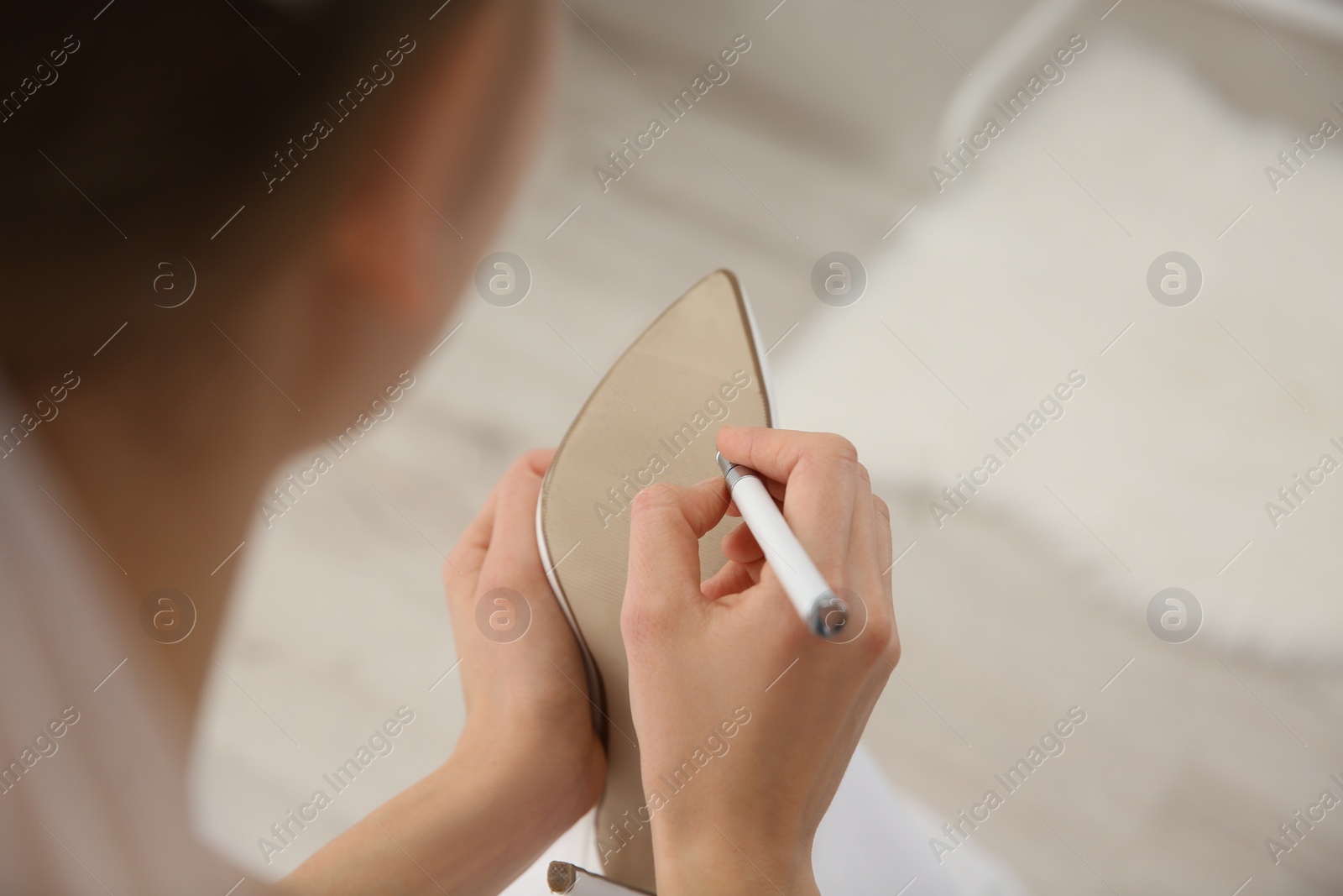 Photo of Young bride writing on her shoe indoors, closeup. Wedding superstition