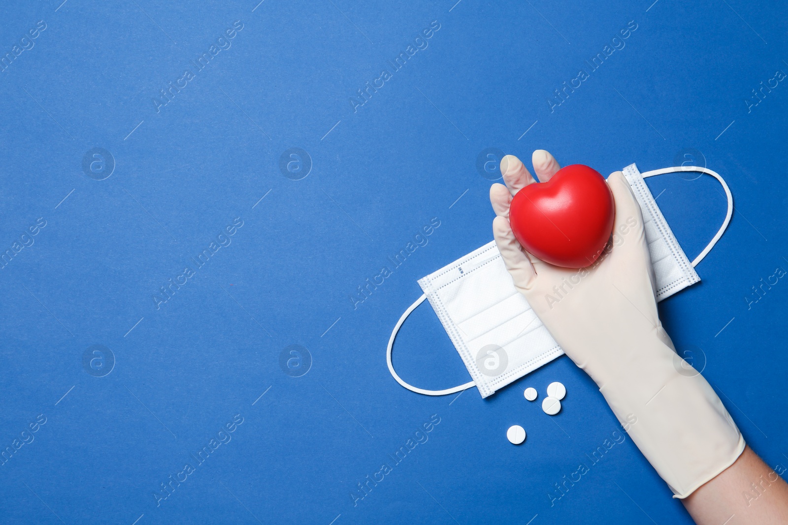 Photo of Doctor in medical glove holding heart on color background, top view. Space for text