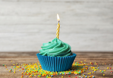 Delicious birthday cupcake with cream and burning candle on wooden table