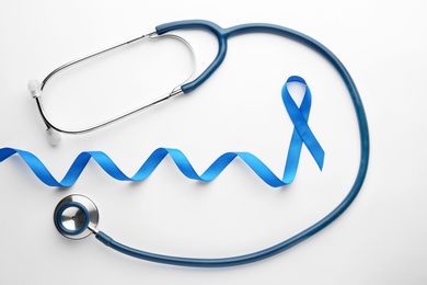 Photo of Blue awareness ribbon and stethoscope isolated on white, top view. Symbol of medical issues