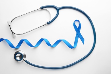 Blue awareness ribbon and stethoscope isolated on white, top view. Symbol of medical issues