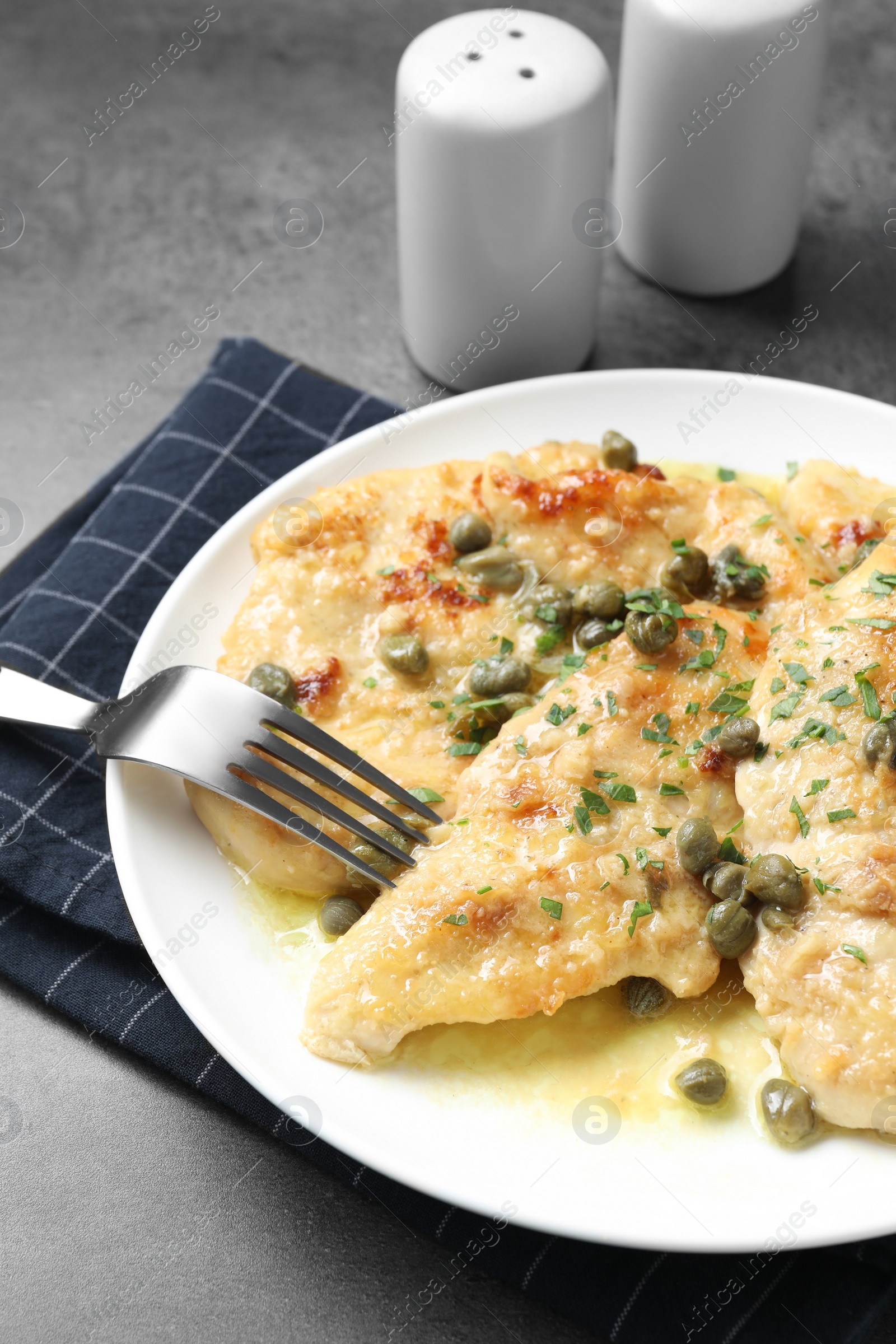 Photo of Delicious chicken piccata with herbs served on grey table