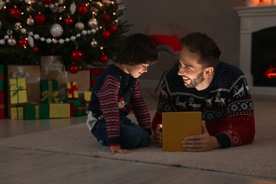 Photo of Father and his cute son opening gift box with magical light on floor at home. Christmas celebration