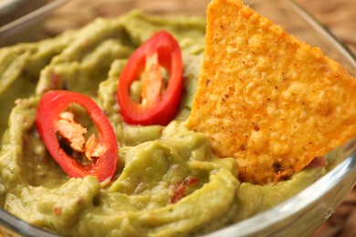 Photo of Delicious guacamole with chili pepper and nachos chip in bowl, closeup