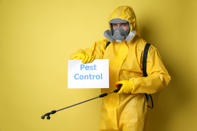 Photo of Man wearing protective suit with insecticide sprayer holding sign PEST CONTROL on yellow background
