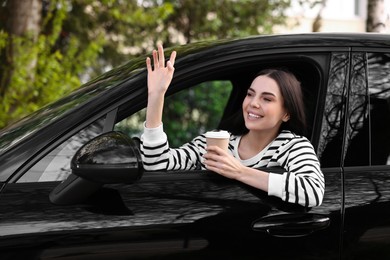 Photo of Young woman with cup of coffee sitting inside her modern car