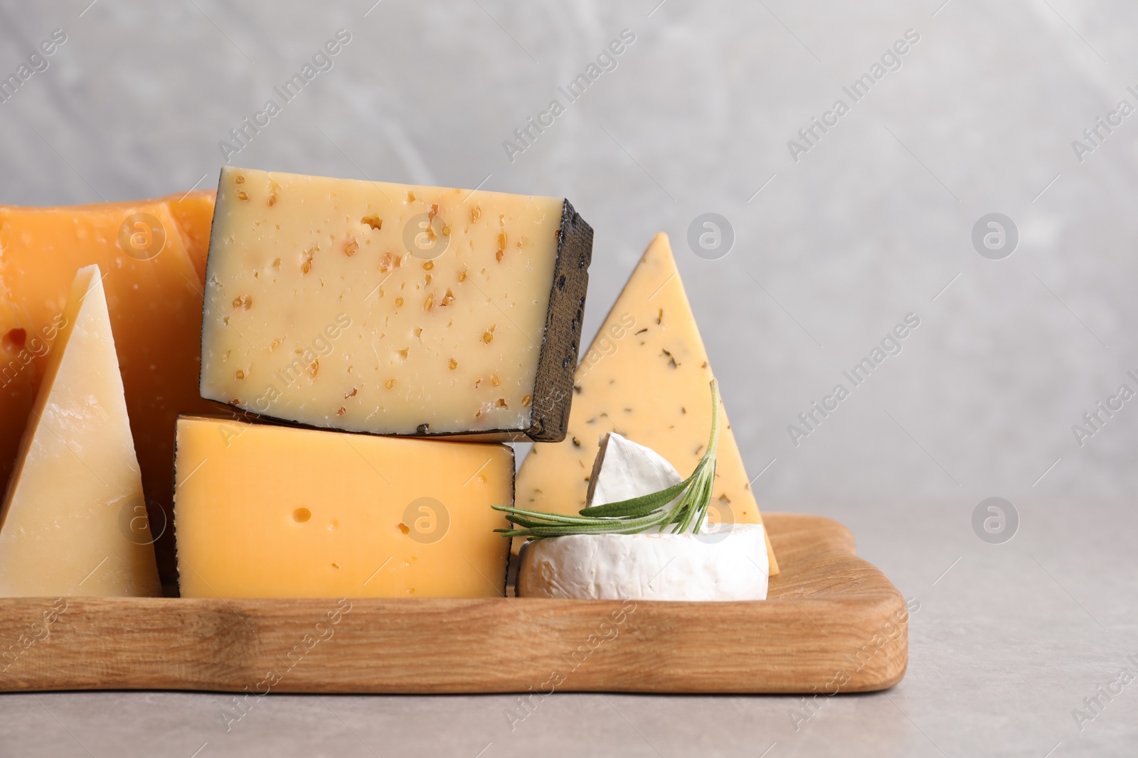 Photo of Wooden tray with different sorts of cheese and rosemary on grey table, space for text