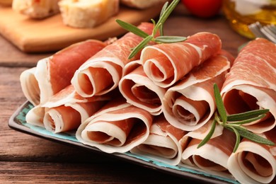 Rolled slices of delicious jamon with rosemary on table, closeup