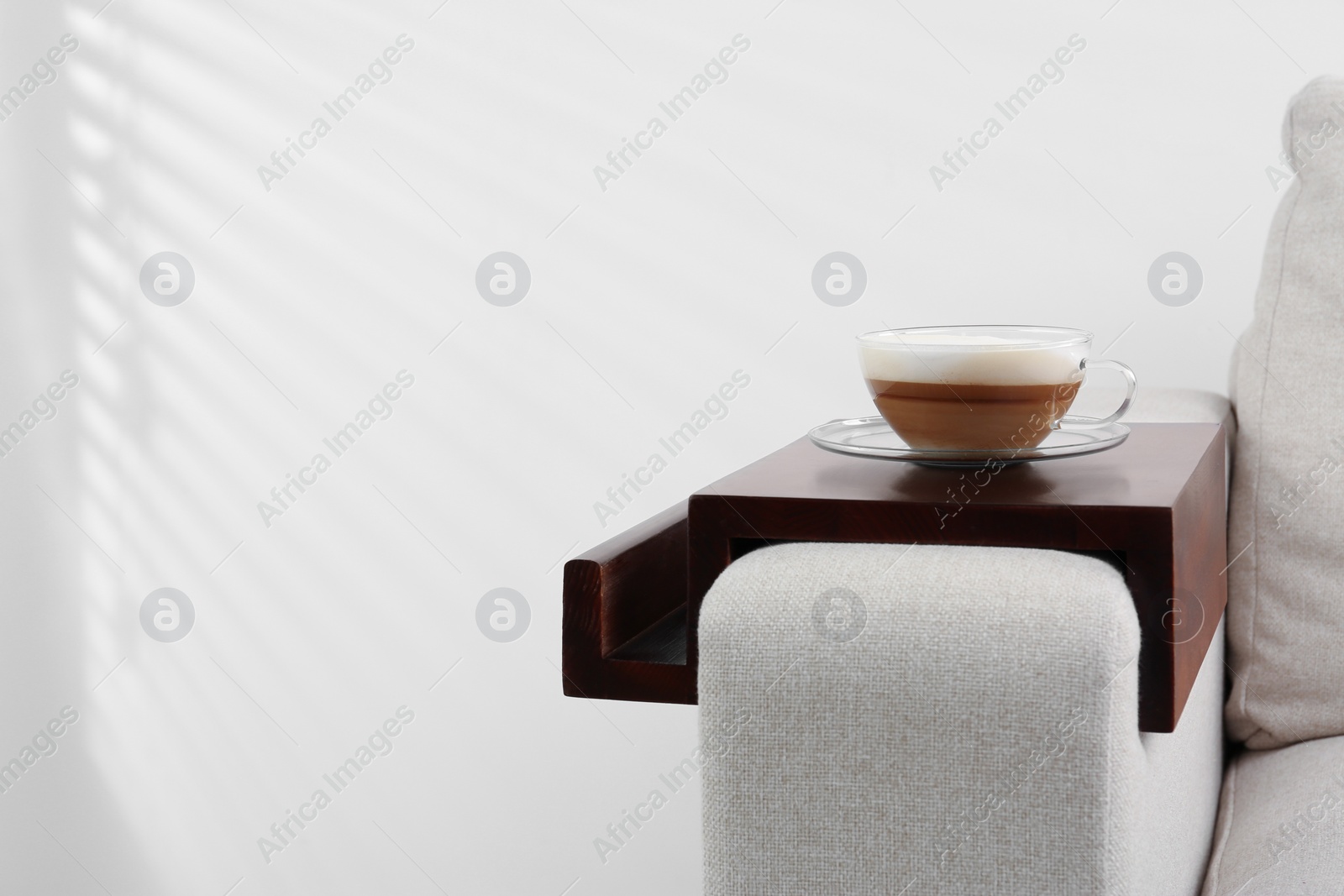 Photo of Cup of coffee on sofa with wooden armrest table indoors, space for text. Interior element