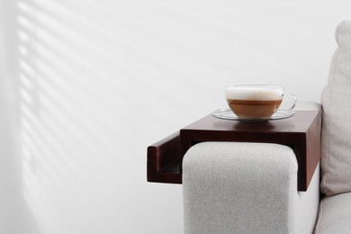 Cup of coffee on sofa with wooden armrest table indoors, space for text. Interior element