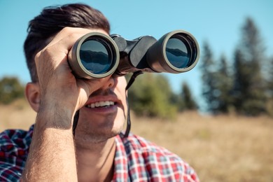 Photo of Man looking through binoculars outdoors on sunny day