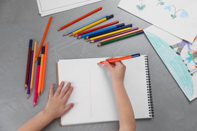 Little boy drawing with pencil at grey textured table, top view. Child`s art