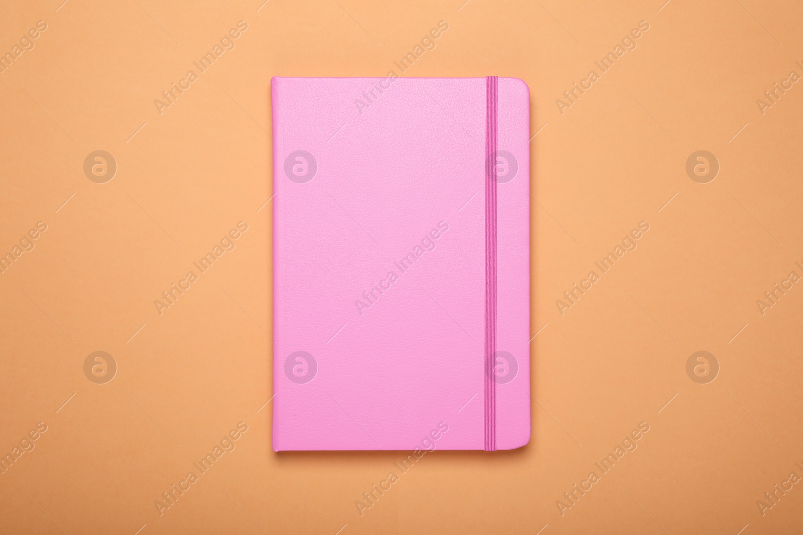 Photo of Closed pink office notebook on pale orange background, top view