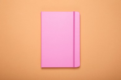 Photo of Closed pink office notebook on pale orange background, top view