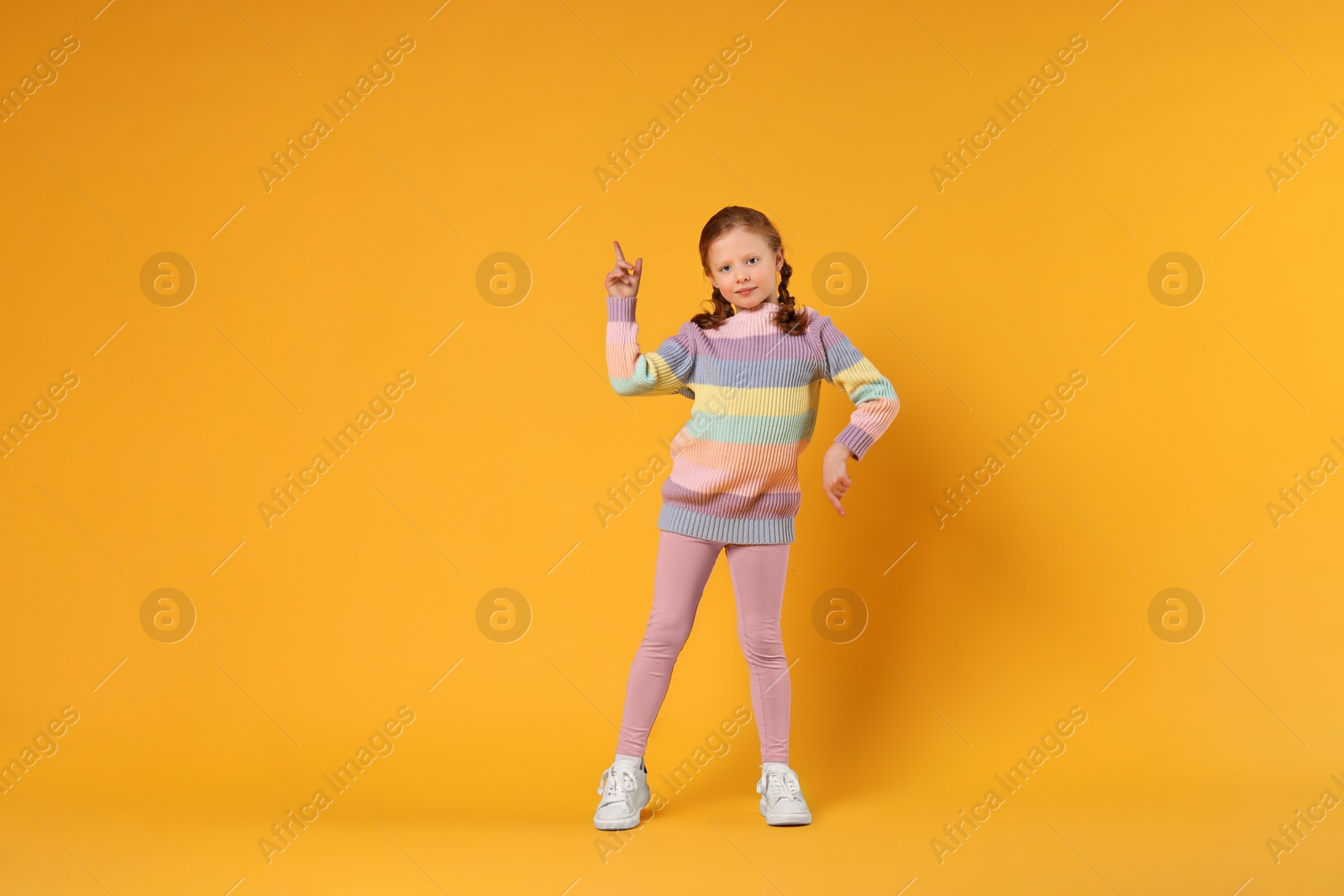 Photo of Cute little girl dancing on orange background