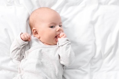Photo of Cute little baby lying on white sheets, top view. Space for text