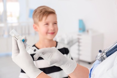 Doctor filling syringe with medicine and child on background. Vaccination day