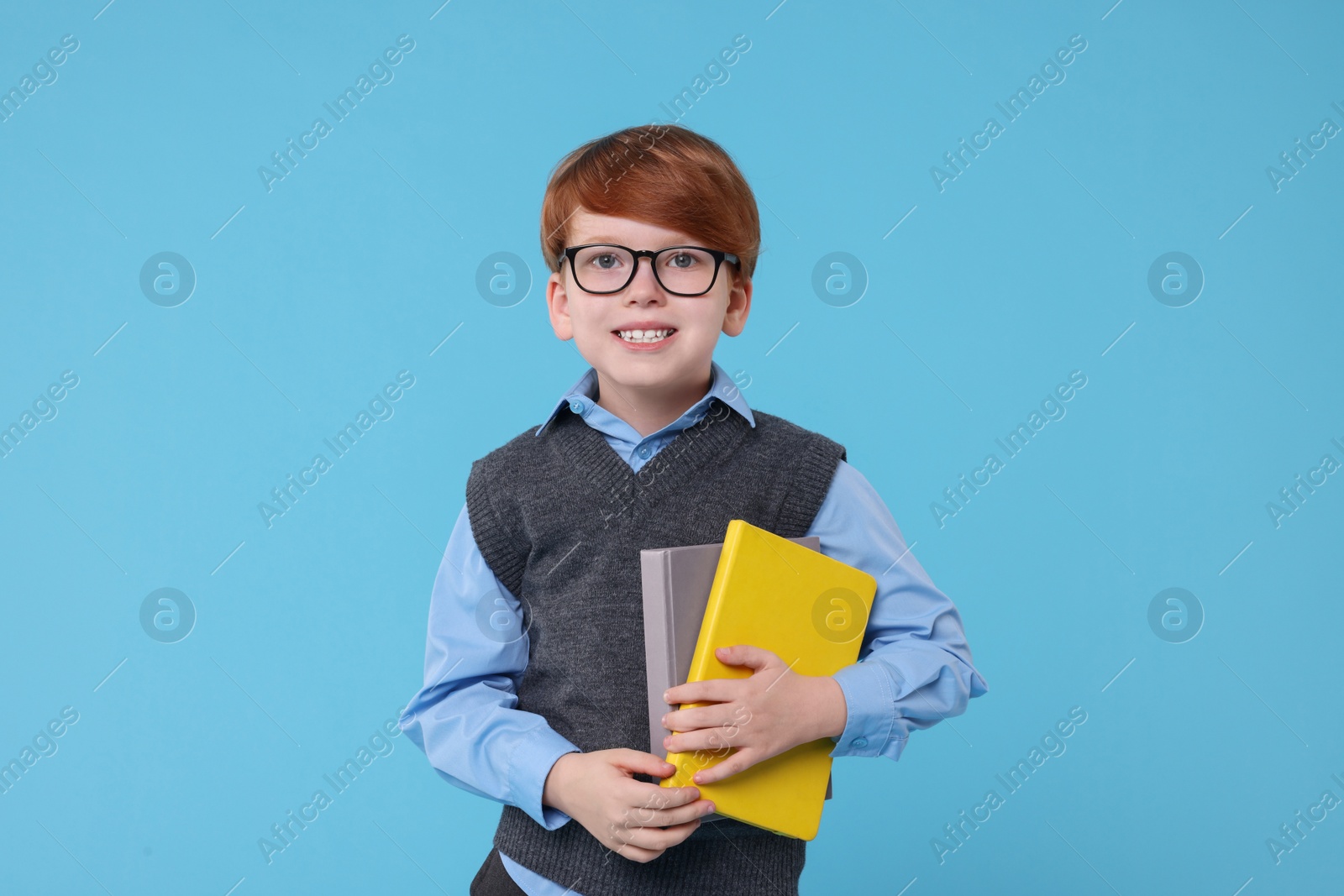 Photo of Smiling schoolboy in glasses with books on light blue background