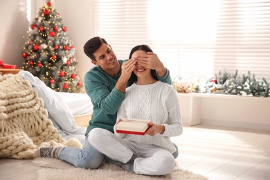 Photo of Happy couple with gift on floor indoors. Christmas celebration