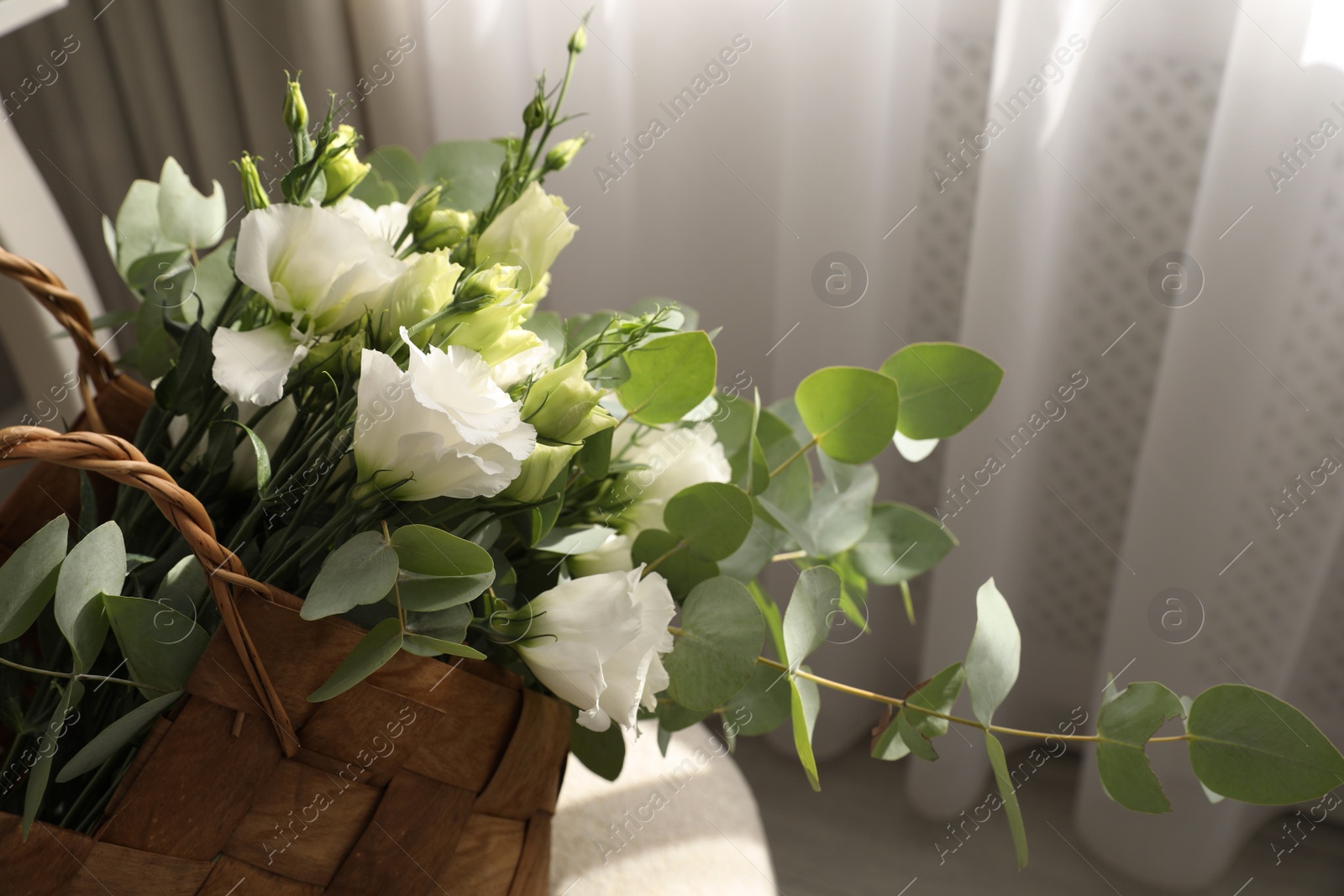Photo of Stylish wicker basket with bouquet of flowers in room, closeup