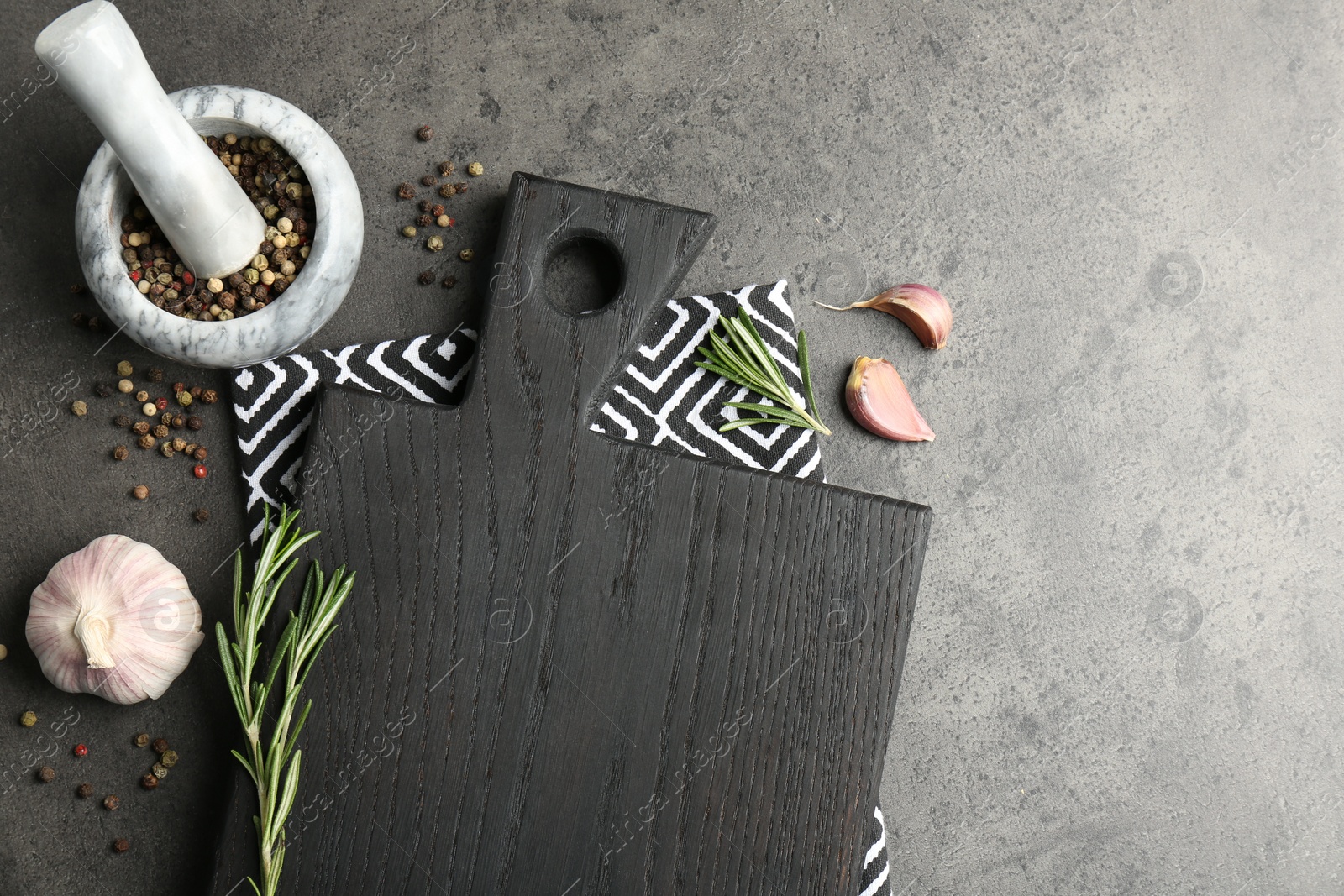 Photo of Black cutting board, napkin and spices on grey table, flat lay. Space for text