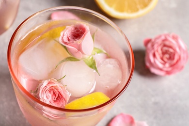 Photo of Tasty refreshing lemon drink with roses on light grey table, closeup