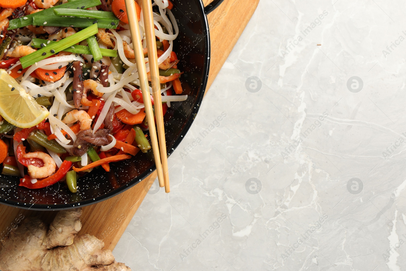 Photo of Shrimp stir fry with noodles and vegetables in wok on grey table, top view. Space for text