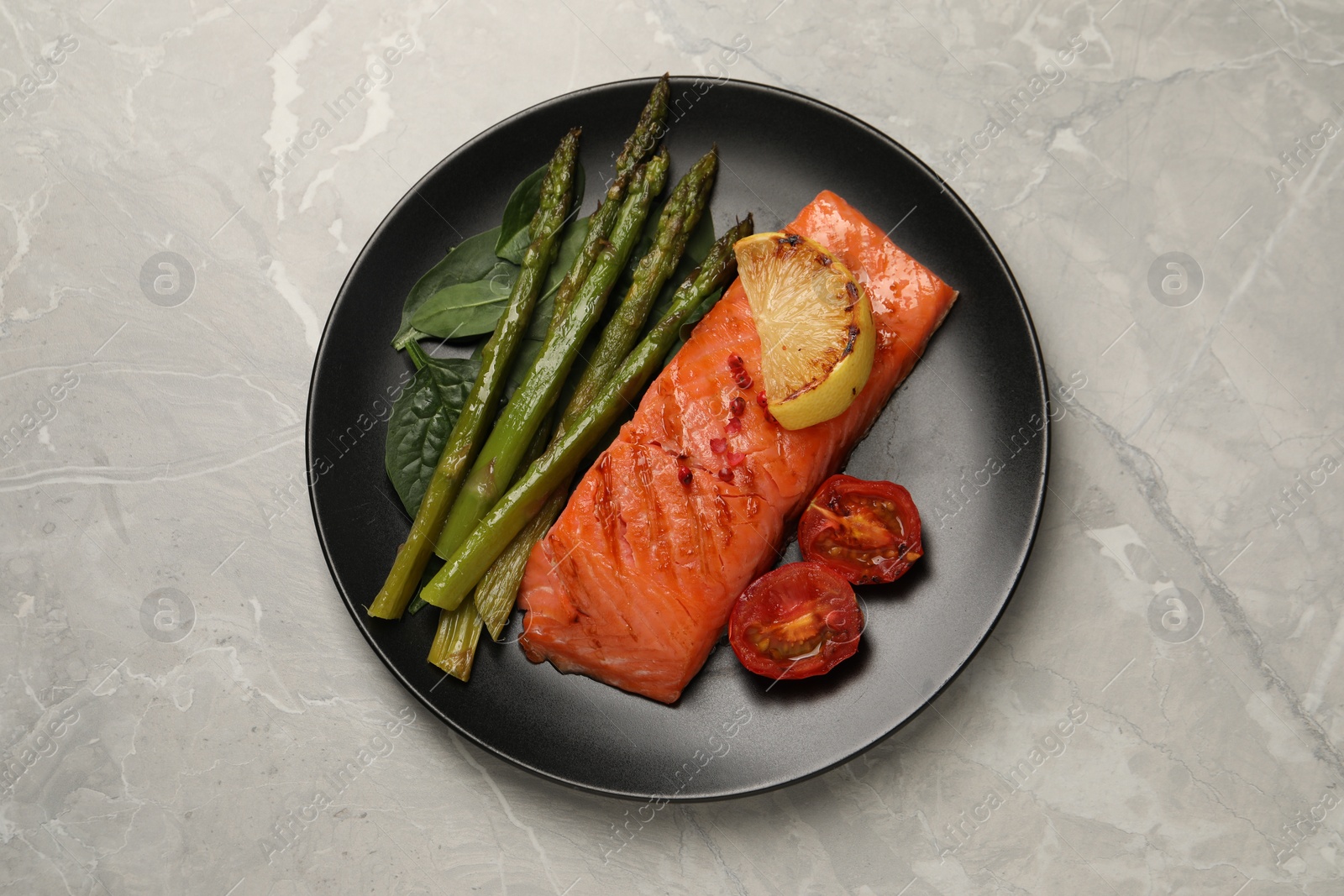 Photo of Tasty grilled salmon with tomatoes, lemon and asparagus on grey table, top view