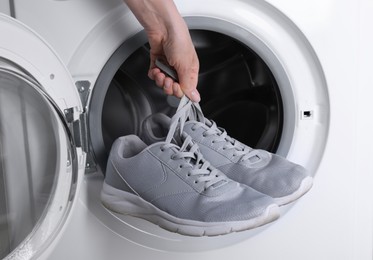 Photo of Woman putting pair of sport shoes into washing machine, closeup