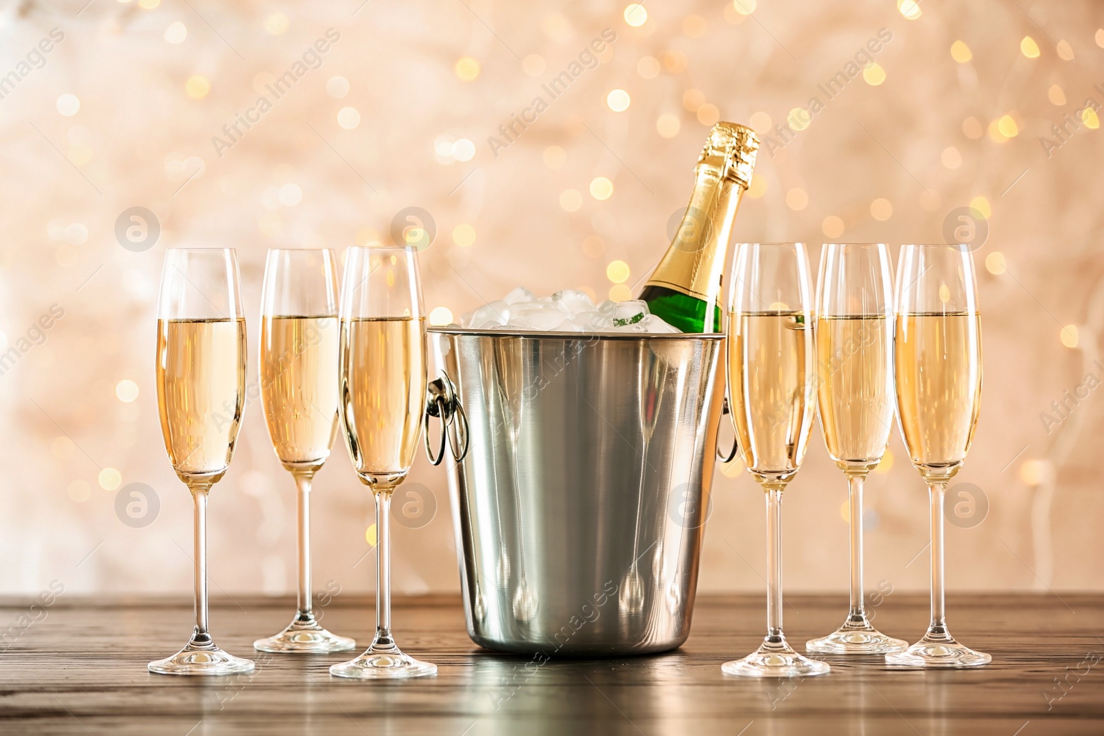 Photo of Glasses with champagne and bottle in bucket on table against blurred lights