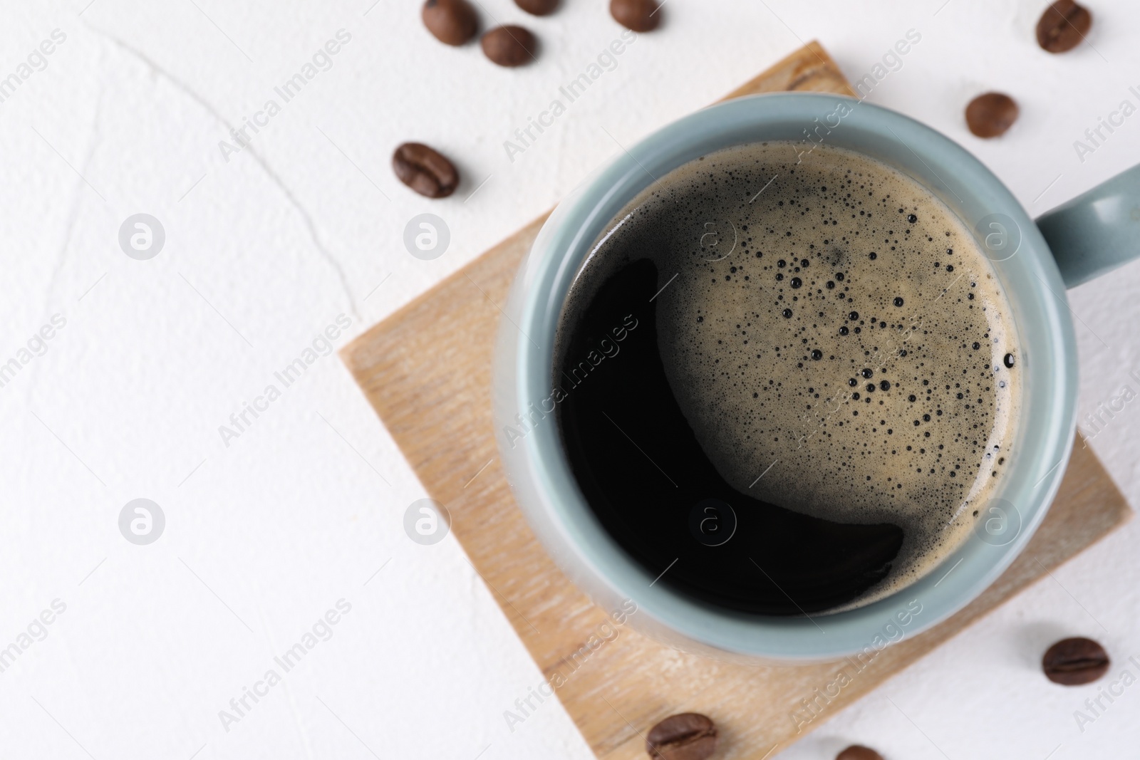 Photo of Delicious coffee in cup and beans on white textured table, top view. Space for text