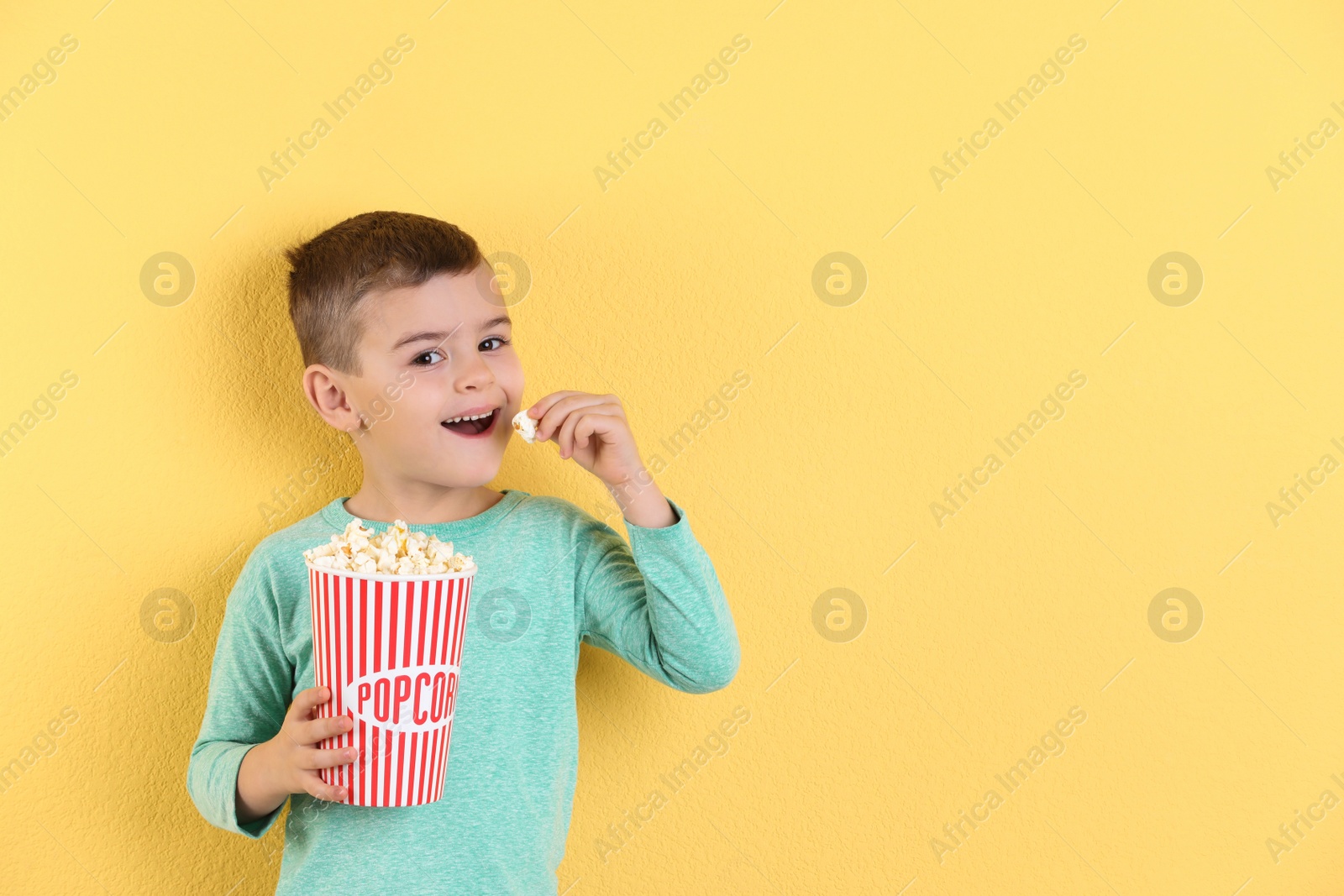 Photo of Cute little boy with popcorn on color background. Space for text