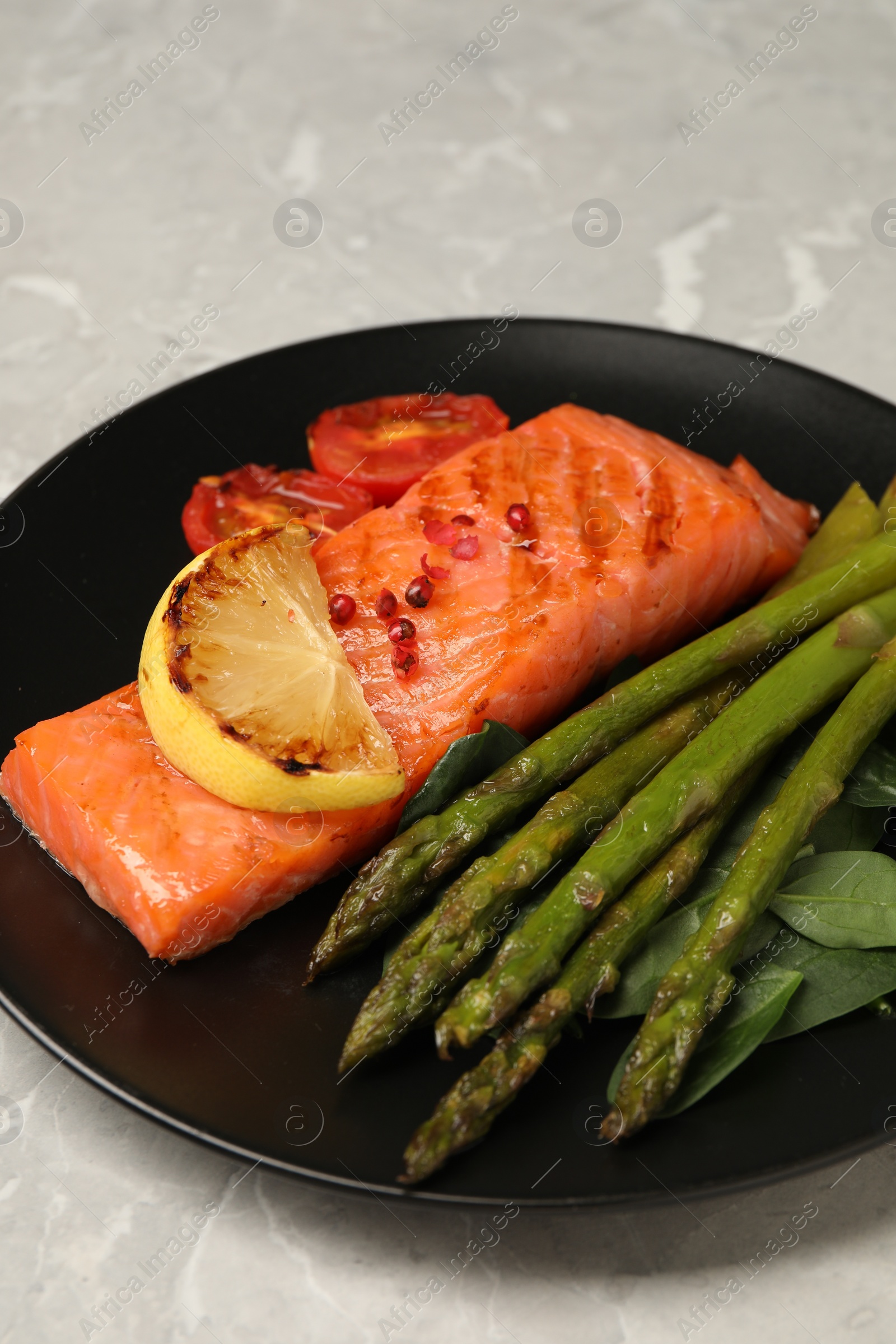 Photo of Tasty grilled salmon with tomatoes, lemon and asparagus on grey table