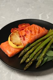 Photo of Tasty grilled salmon with tomatoes, lemon and asparagus on grey table