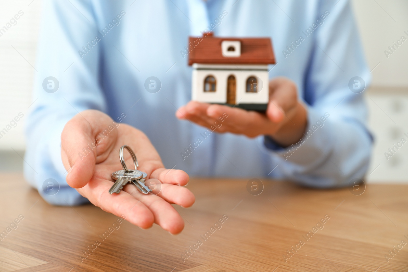 Photo of Real estate agent holding house model and keys at wooden table, closeup