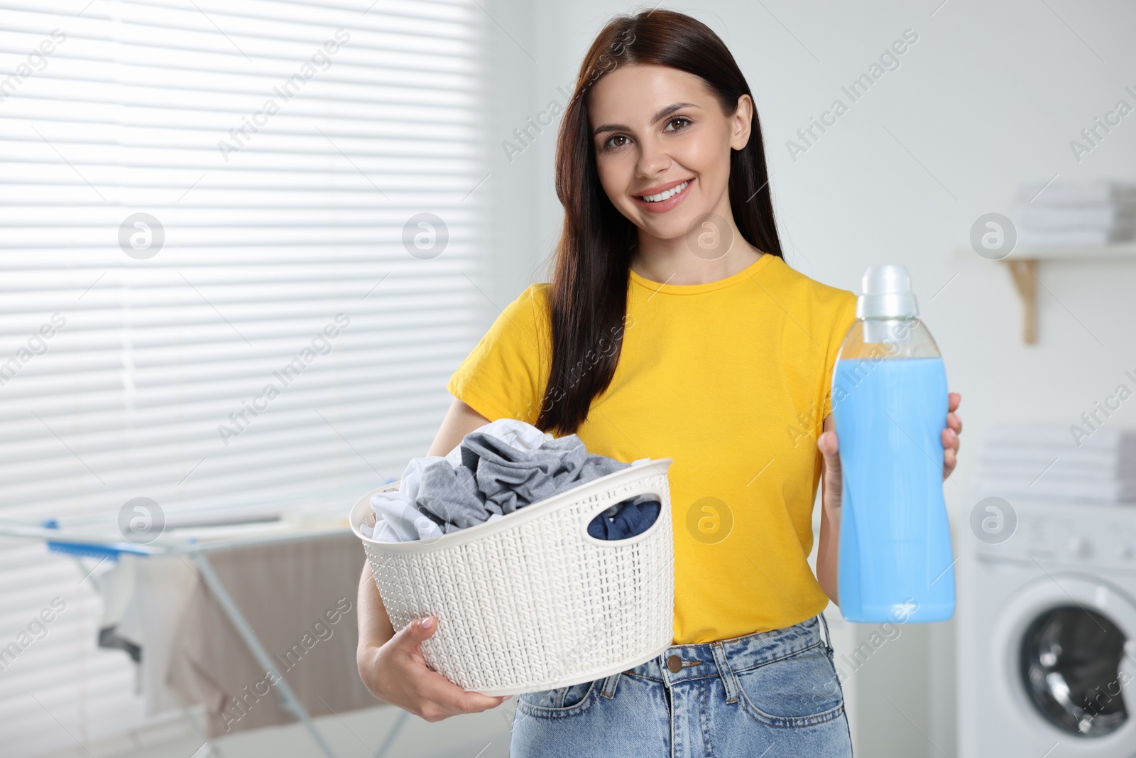 Photo of Woman holding basket with dirty clothes and fabric softener in bathroom, space for text