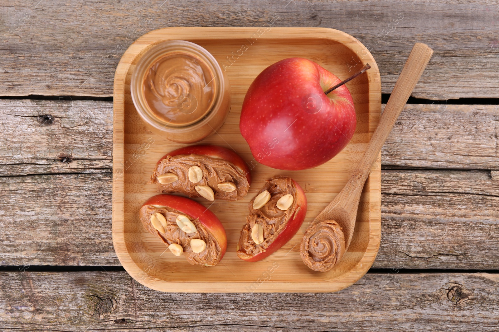 Photo of Fresh apples with peanut butter and spoon on wooden table, top view