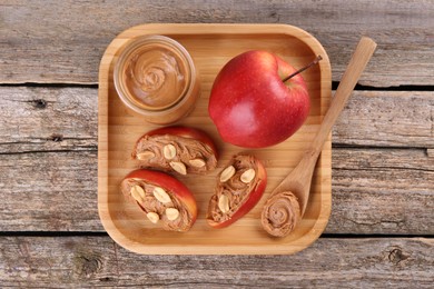 Fresh apples with peanut butter and spoon on wooden table, top view