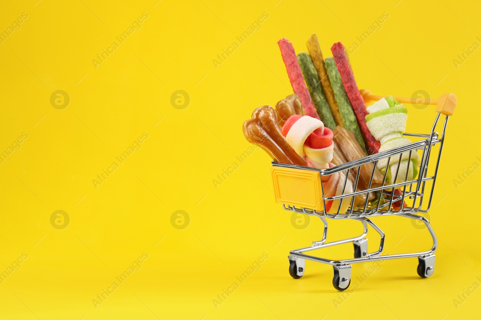 Photo of Small shopping cart with different pet goods on yellow background, space for text. Shop assortment