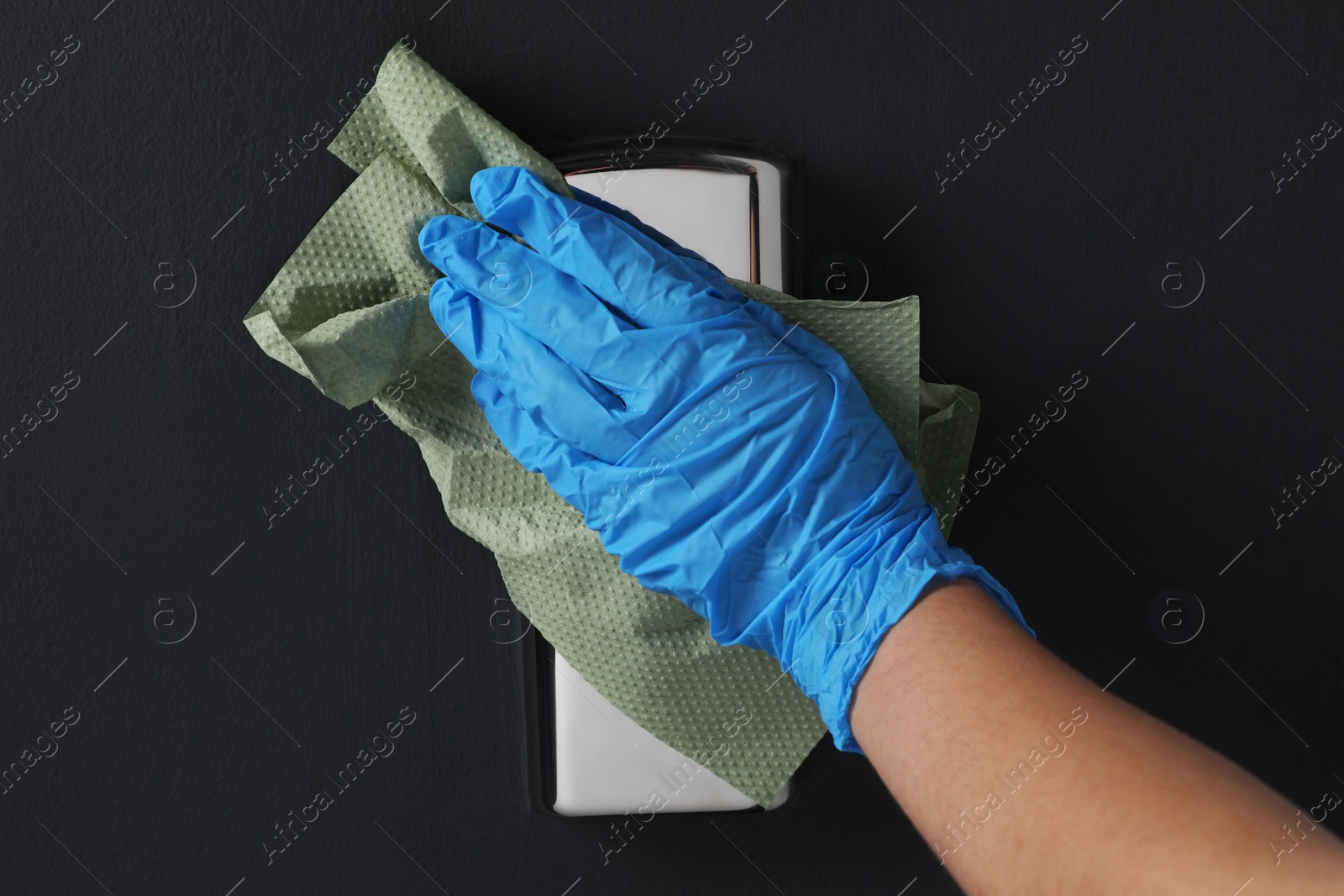 Photo of Woman in glove cleaning elevator button with paper towel indoors, closeup