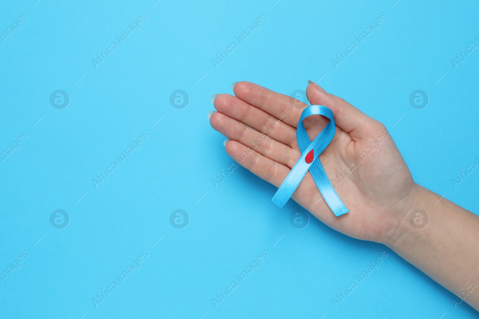 Photo of Woman holding light blue ribbon with paper blood drop on color background, top view and space for text. Diabetes awareness