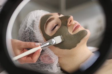 Photo of Cosmetologist applying mask on woman's face, closeup