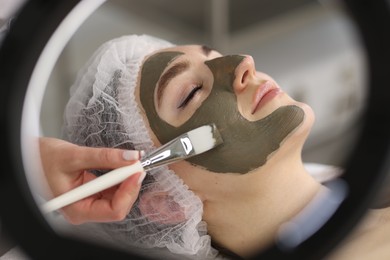 Cosmetologist applying mask on woman's face, closeup