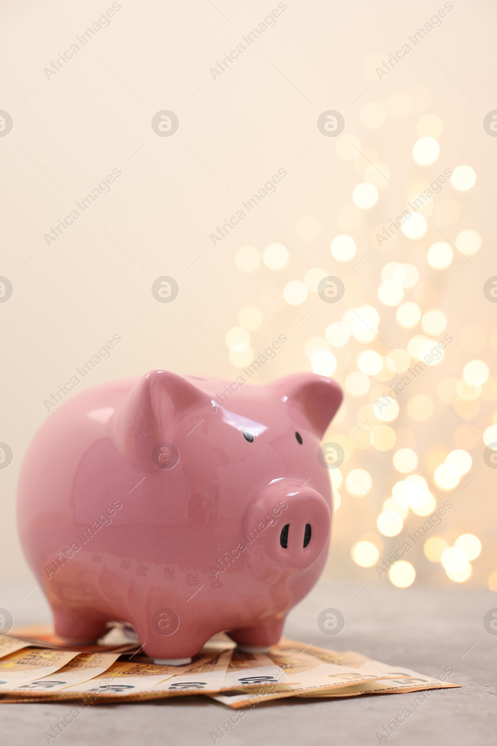 Photo of Piggy bank with euro banknotes on grey table against blurred lights, space for text